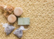 Natural spa products displayed on a woven mat, including a green soap bar, two wooden caps, and lavender sachets."