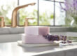 Lavender-infused handmade soaps stacked on a marble tray next to fresh lavender sprigs, with a sunny window and modern kitchen sink in the background.